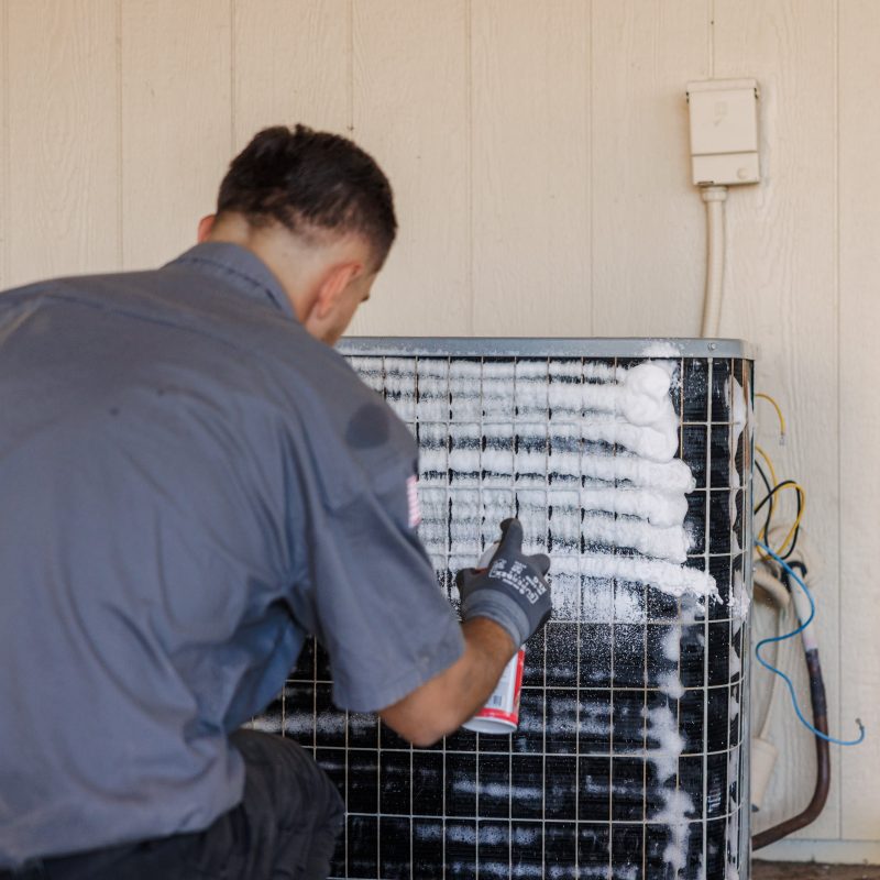 Technician cleans foamy outdoor air conditioner condenser coils